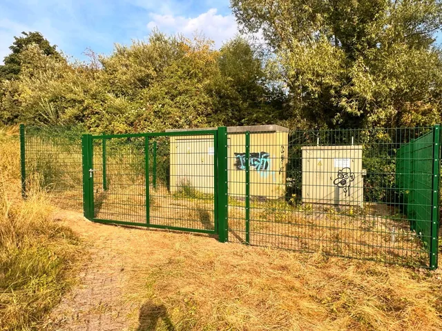Grün beschichteter Gitterzaun mit Tor als Zugang zu einem Grundstück
